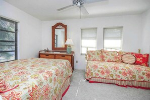 A bedroom with two beds, a dresser, a mirror, and a ceiling fan.