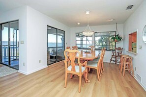A dining area with a wooden table and chairs, large windows with a view, and a chandelier.