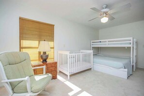 A child's room with bunk beds, a crib, a chair, a lamp, and a ceiling fan. - Waterside Retreat with Pool, Steps to Lighthouse (Sanibel)