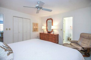 Une chambre à coucher comprenant un lit, une commode, une chaise, un ventilateur de plafond et une porte donnant sur une autre pièce.