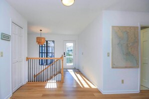 A hallway with a wooden staircase, a hanging light fixture, and a map on the wall. - Waterside Retreat with Pool, Steps to Lighthouse (Sanibel)