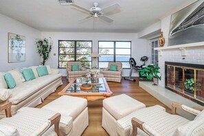 A spacious living room with a sofa, chairs, a coffee table, a fireplace, and large windows. - Waterside Retreat with Pool, Steps to Lighthouse (Sanibel)