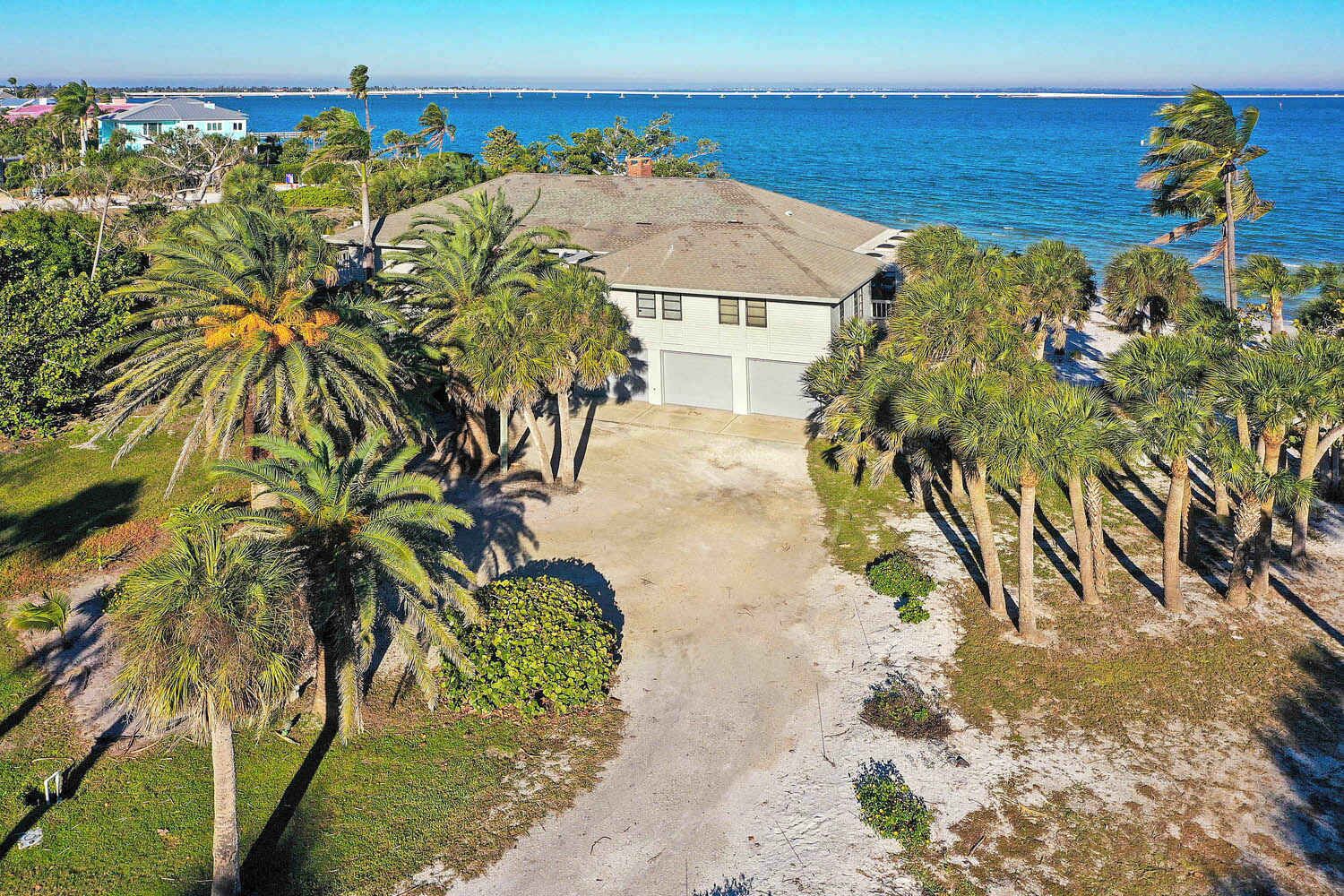 A coastal property with a paved driveway leading to a building, surrounded by palm trees and a view of the ocean.