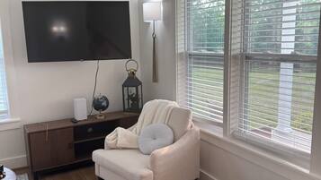 A living room with a flat-screen TV, a lamp, a sofa, and a wicker ottoman.