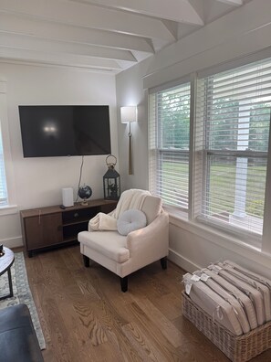 A living room with a flat-screen TV, a lamp, a sofa, and a wicker ottoman.