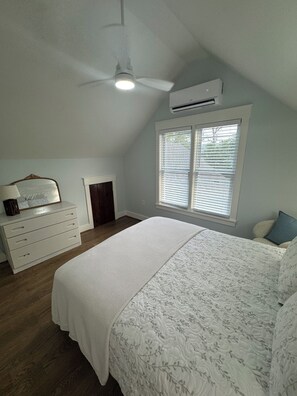 A bedroom with a bed, dresser, window with blinds, ceiling fan, and air conditioning unit.