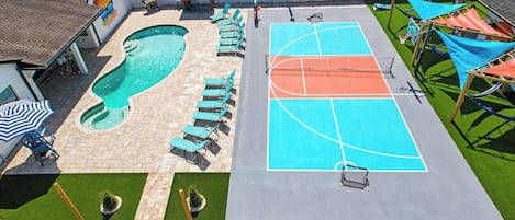 Una piscina al aire libre con sillones de descanso, una cancha de baloncesto y un pequeño jardín.