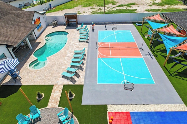 An outdoor swimming pool with lounge chairs, a basketball court, and a small garden area.
