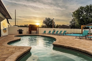 A swimming pool with a curved design, surrounded by lounge chairs and a patio area.