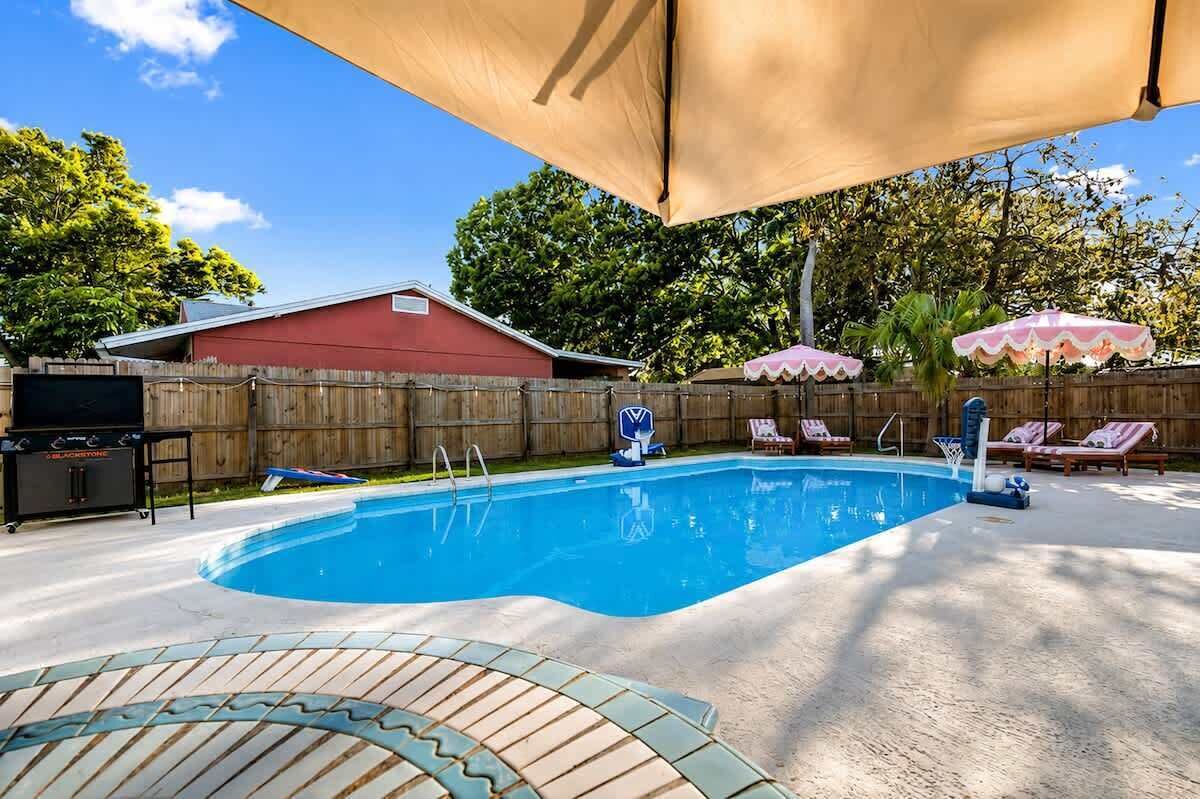 A backyard with a swimming pool, lounge chairs, and a covered area.