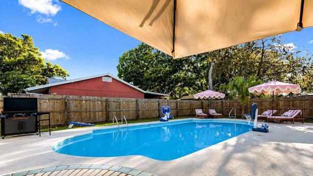 Ein Garten mit Schwimmbad, Liegestühlen und einer überdachten Terrasse.