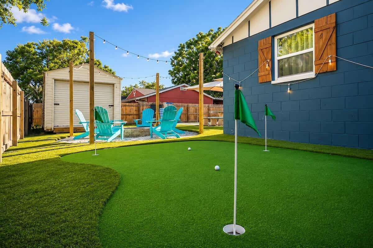 Un patio con césped sintético, un putting green y dos sillas de jardín verdes.