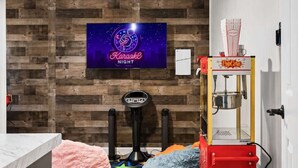 Ein Raum mit Holzwand, einem Neon-Schild für Karaoke-Nacht, einer Popcorntheke und Trainingsgeräten.
