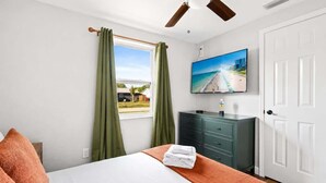 Ein Hotelzimmer mit einem Bett, einem Fernseher, einem Fenster mit Vorhängen, einem Deckenventilator und einer Tür.
