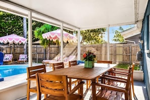 A covered patio with a wooden table and chairs, a pool, and umbrellas. - Heated Pool • Golf • Fire Pit • 15 Min To Beach (Seminole)