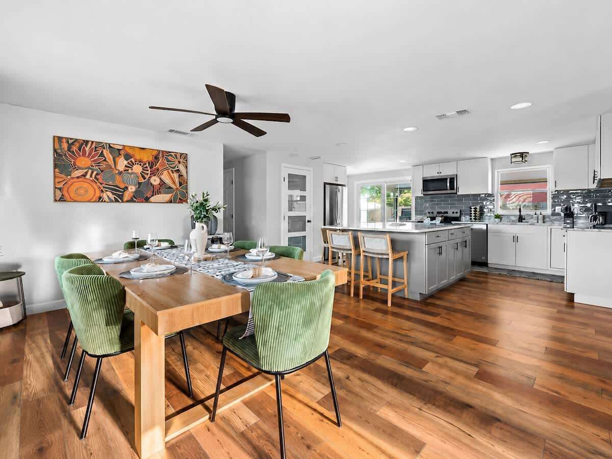 A modern kitchen with a dining area, wooden flooring, and a ceiling fan.