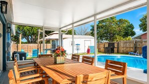Ein überdachter Patio-Bereich mit Holztisch und -stühlen, einem Pool und einem weißen Wohnmobil im Hintergrund.