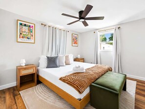 Une chambre à coucher avec un lit, des tables de chevet, un ventilateur de plafond et une fenêtre avec des rideaux.