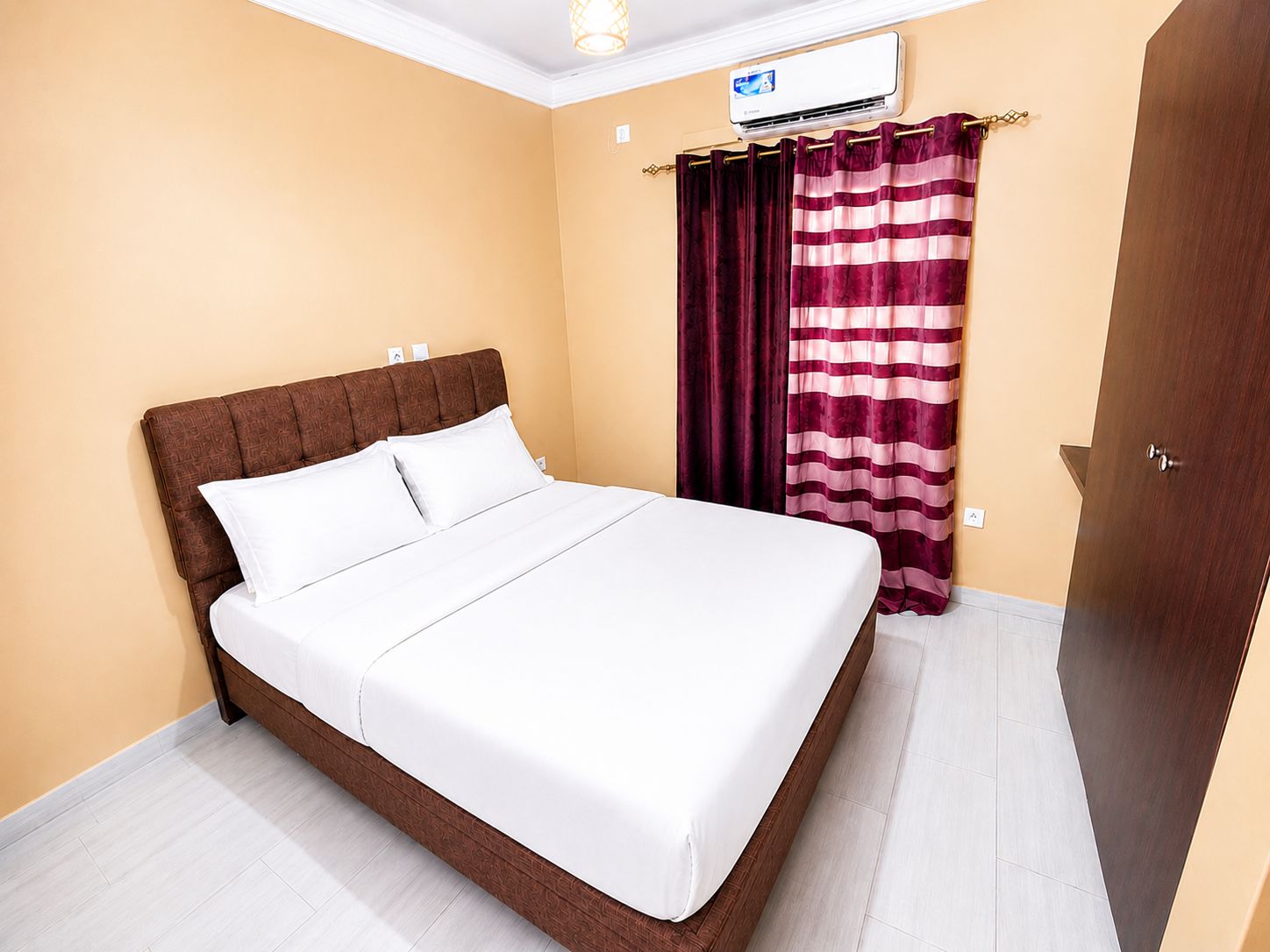 A hotel room with a bed, curtains, an air conditioning unit, and a door.