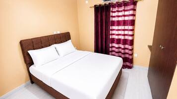A hotel room with a bed, curtains, an air conditioning unit, and a door.