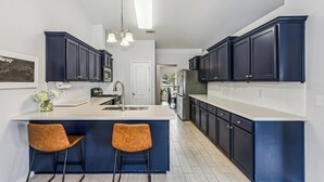 A modern kitchen with dark cabinetry, a central island with bar stools, and a pendant light fixture. - Spacious 4-bedroom house in serene Pensacola with private pool (Pensacola)
