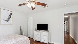 A bedroom with a bed, a dresser, a television, and a ceiling fan. - Spacious 4-bedroom house in serene Pensacola with private pool (Pensacola)