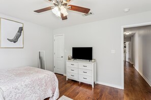 Ein Schlafzimmer mit einem Bett, einem Schminktisch, einem Fernseher und einem Deckenventilator.