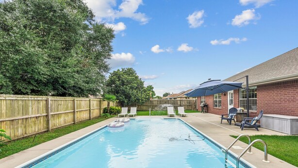 A rectangular swimming pool with a tiled edge, surrounded by a wooden fence, and adjacent to a brick building with a covered patio area. - Spacious 4-bedroom house in serene Pensacola with private pool (Pensacola)