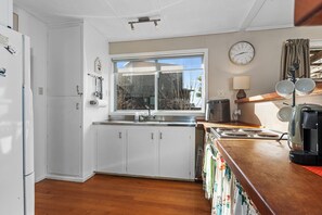 Une cuisine avec des meubles blancs, une fenêtre, un évier, une cuisinière et une horloge au mur.