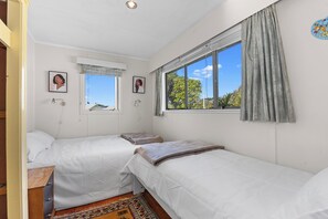 A bedroom with two beds, a window with curtains, and two wall-mounted lamps. - Coastal Hideaway - Waipu Cove Holiday Home (Waipu)