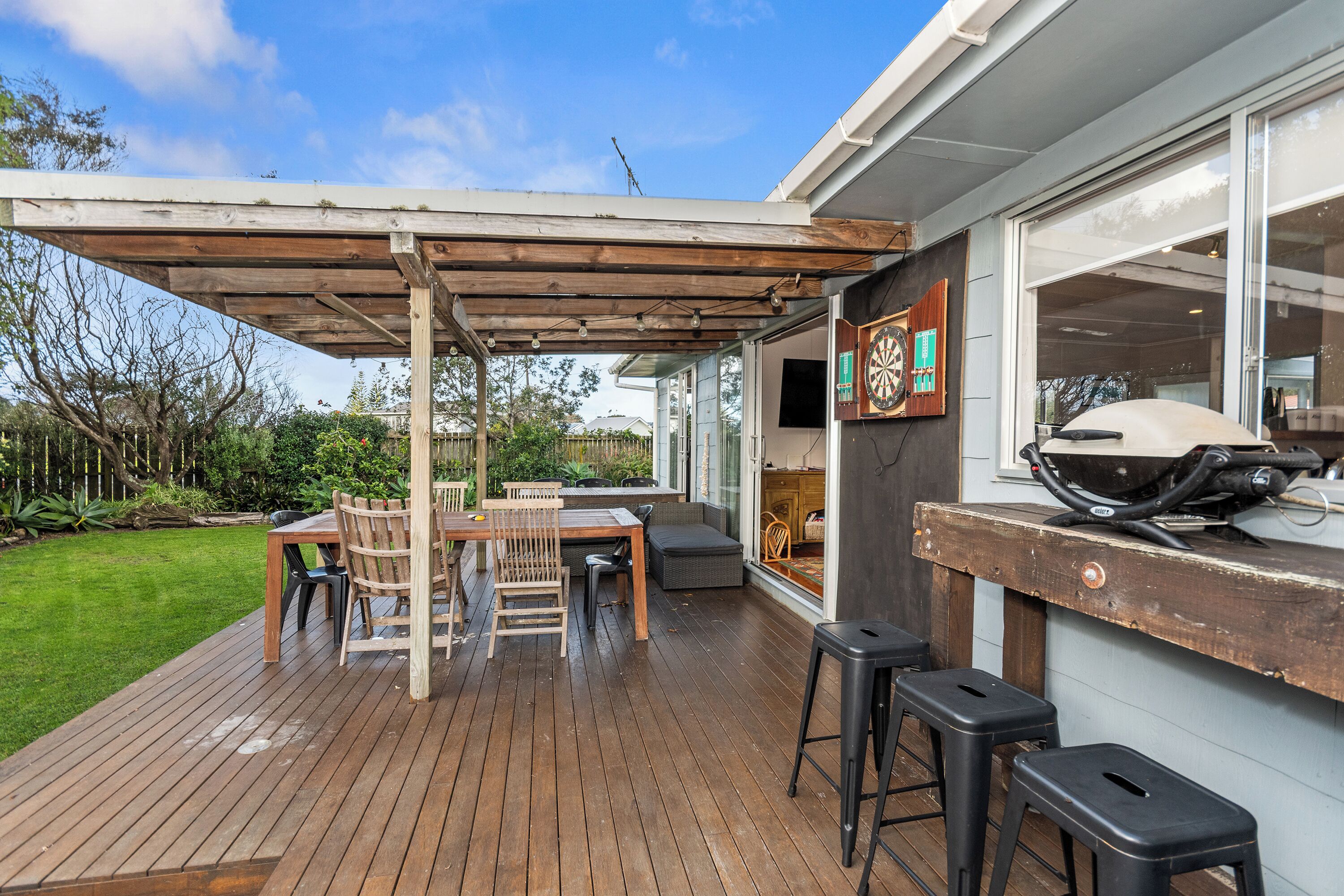 An outdoor patio area with a wooden deck, a covered seating area, and a barbecue grill.