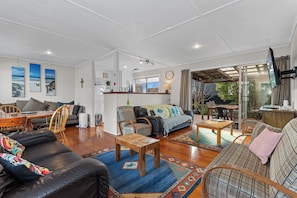 A spacious living area with a sofa, chairs, a coffee table, and a television. - Coastal Hideaway - Waipu Cove Holiday Home (Waipu)