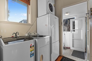 A compact kitchen with a washing machine, a sink, and a door leading to another room. - Coastal Hideaway - Waipu Cove Holiday Home (Waipu)