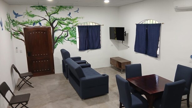 A room with a wooden door, blue curtains, a flat-screen TV, a small wooden cabinet, and a dining table with chairs. - Vila #3, spacious private villa fits 7 people w/ AC in gorgeous La Costa del Sol (San Pedro Masahuat)