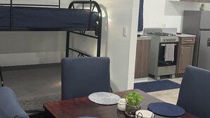 A compact room with a bunk bed, a dining table with chairs, a kitchen area with a stove and refrigerator, and a small potted plant. - Vila #3, spacious private villa fits 7 people w/ AC in gorgeous La Costa del Sol (San Pedro Masahuat)