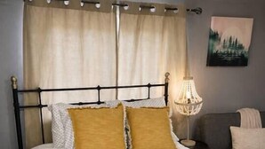 Una cama con estructura metálica negra, ropa de cama blanca y dos almohadas color mostaza.