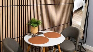 Una habitación moderna con un televisor de pantalla plana montado en una pared de listones de madera, una mesa redonda con dos sillas y un espejo grande en la pared.