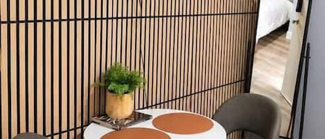 Une chambre moderne avec un téléviseur à écran plat fixé sur un mur en lambris de bois, une table ronde avec deux chaises et un grand miroir sur le mur.