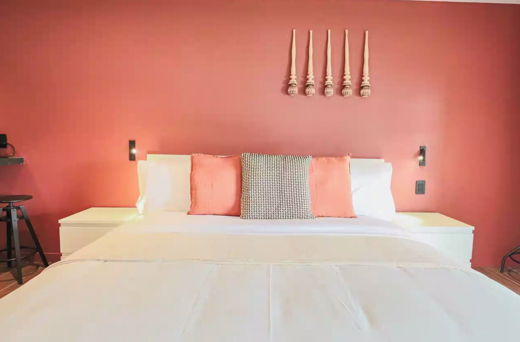 A bed with white bedding, a patterned pillow, and a red wall with a wall-mounted light fixture.