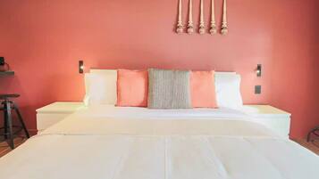 A bed with white bedding, a patterned pillow, and a red wall with a wall-mounted light fixture.