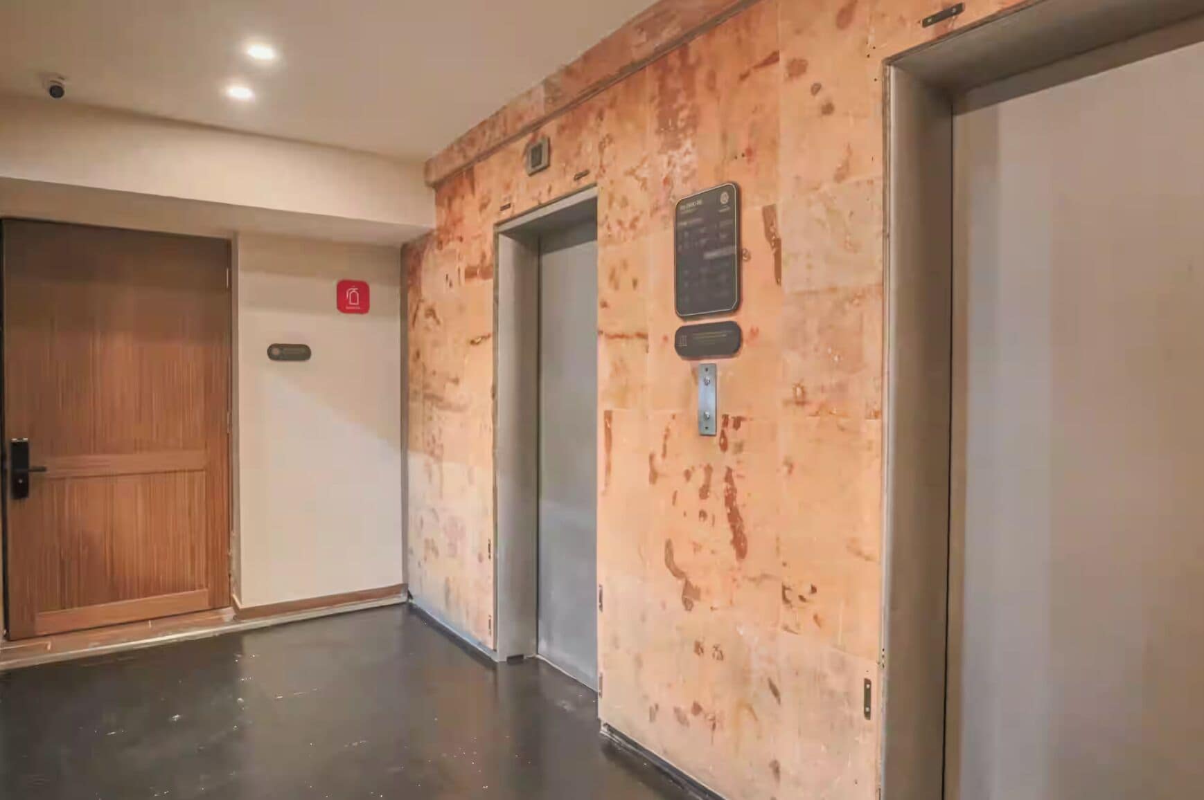 Un pasillo con puerta de madera, un ascensor y un cartel en la pared.