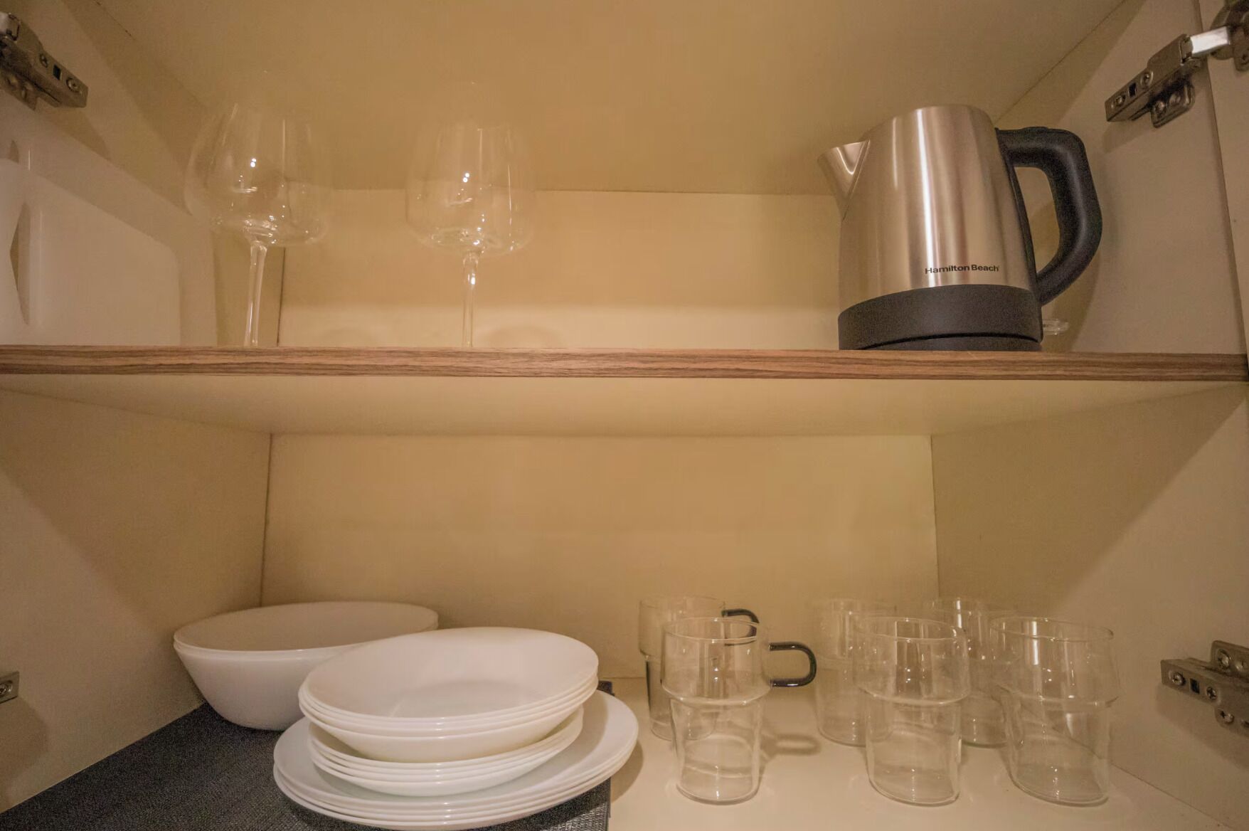 A kitchen area with a coffee maker, wine glasses, and stacked plates and cups.