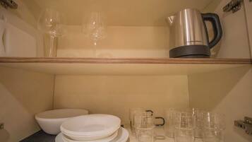 A kitchen area with a coffee maker, wine glasses, and stacked plates and cups.