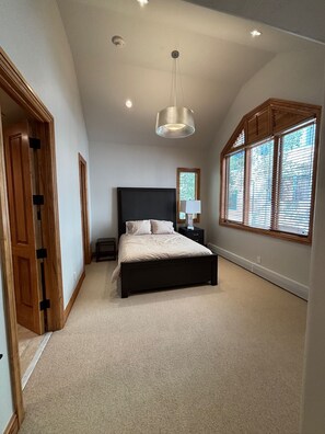Een slaapkamer met een groot bed, een plafondlamp, een nachtkastje en een raam met jaloezieën.
