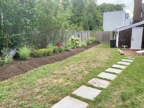 A backyard with a stone pathway, a wooden fence, and various plants. - Walk, East Hampton Village Barn Cottage Furnished cottage mins to Ocean Beaches (East Hampton)