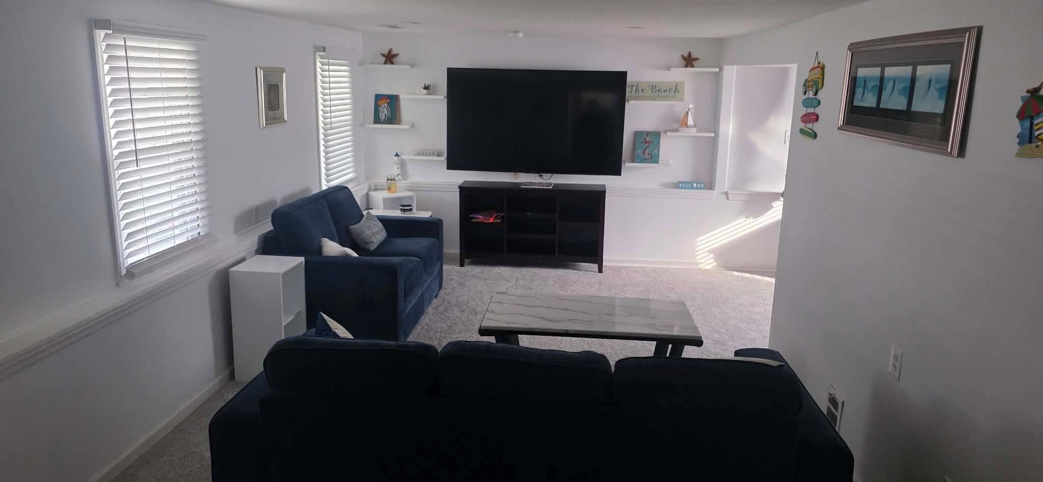 Ein Wohnzimmer mit Flachbildfernseher, einer Couch, einem Couchtisch und einer kleinen Kommode.