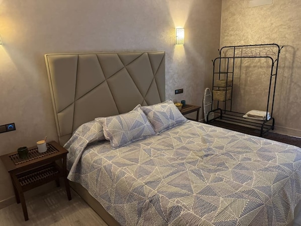 A hotel room with a bed, a bedside table, a lamp, and a metal rack.