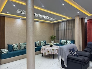 A modern living room with a sofa set, a round table with a floral tablecloth, and a black leather chair.