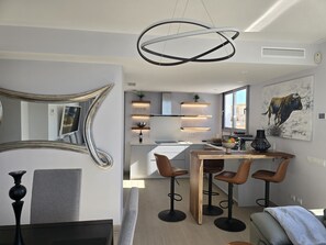 A modern kitchen with built-in appliances, a dining area with stools, and a large mirror.