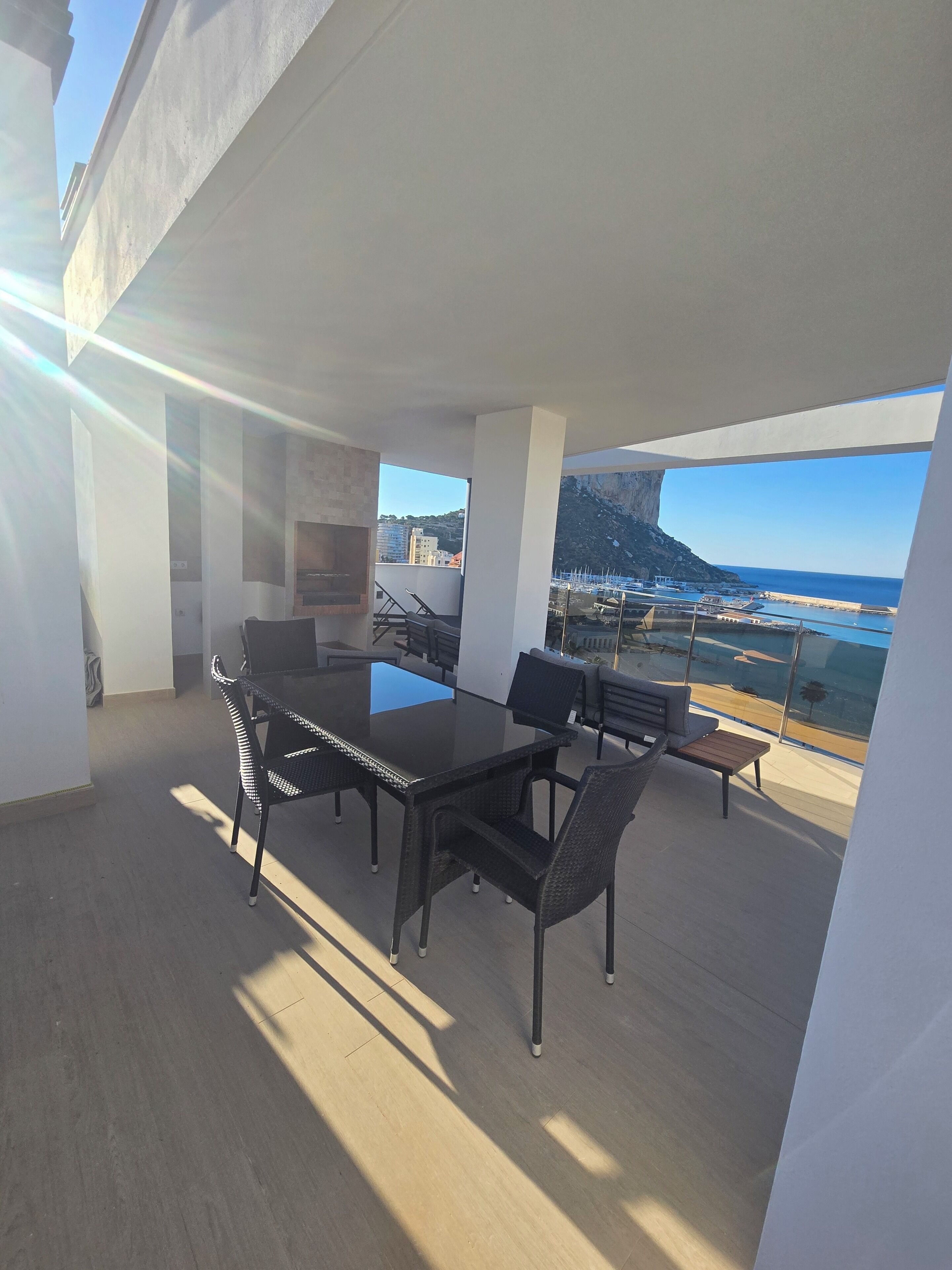 A modern outdoor dining area with a view of the sea and a cliff.